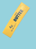 Hand holding a yellow butter container with blue text on a concrete floor.