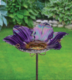 Decorative purple glass flower on a stand against a green garden background