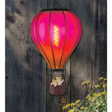 Decorative wall light shaped like a hot air balloon with cats in a basket on a wooden background.