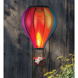 Colorful hot air balloon-shaped light fixture on a wooden wall with flowers in the foreground.