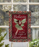 Decorative Christmas flag with fairy design and text 'Believe in the magic of Christmas' hanging in front of a window.