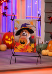 Halloween-themed painting of a dog with a pumpkin and witch hat on an easel, surrounded by pumpkins and decorations.