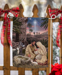 Decorative Christmas banner with a nativity scene hanging on a wooden fence with red ribbons.