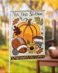 Decorative garden flag with autumn elements and 'Tis the Season text, displayed outdoors.