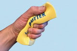 Hand holding a yellow butter container with blue text on a concrete floor.