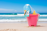 Pink sand bucket set with toys and a blue mesh bag on a white background