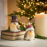 Ceramic Christmas Bird Table Decor featuring birds in festive hats on books with a candle and Christmas tree in the background.
