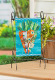Decorative garden flag with carrots on a stand next to a wooden planter with flowers