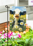 Garden flag with a cow design in a field of flowers, held by a stand outdoors.