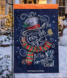 Decorative garden flag with Christmas-themed design featuring a snowman and text, set against a snowy outdoor background.