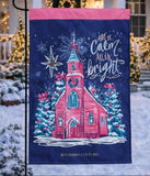 Decorative flag with a church design and 'All is Calm, All is Bright' text in a snowy outdoor setting.