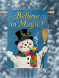 Decorative flag with a snowman holding a broom and smoking a pipe, against a blue background with 'Believe in Magic!' text.