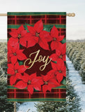 Decorative flag with red poinsettias and 'Joy' text on a plaid background, blurred lights in the background.