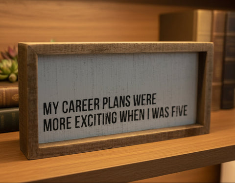 Wooden sign with text on a shelf with books and plants in the background
